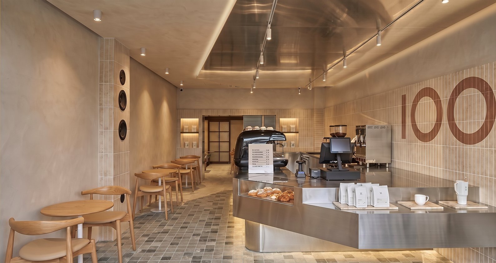 Interior counter and register beneath a stainless-steel canopy beside a beige tile wall with a large '100' graphic