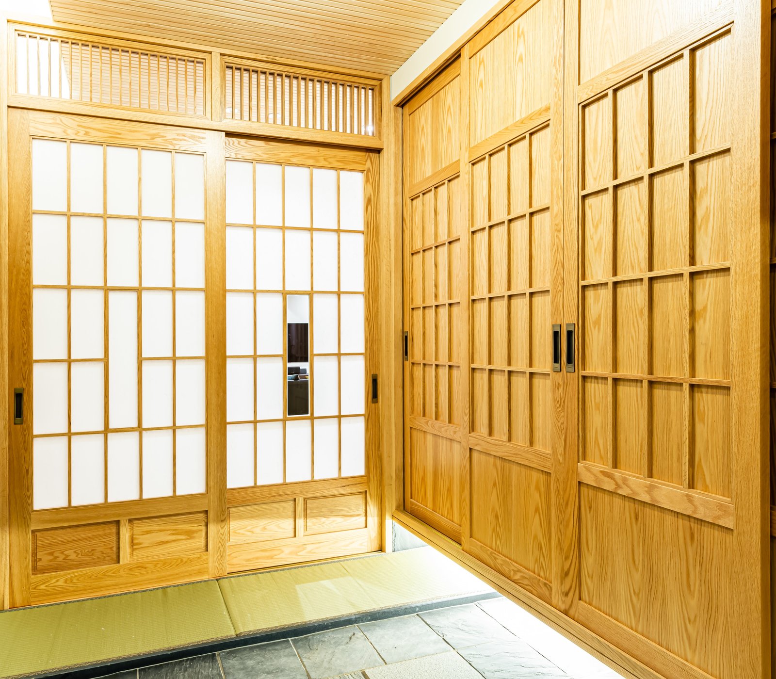 Wide-angle view of shoji sliding doors beside built-in wood closets over a tatami and slate entry floor