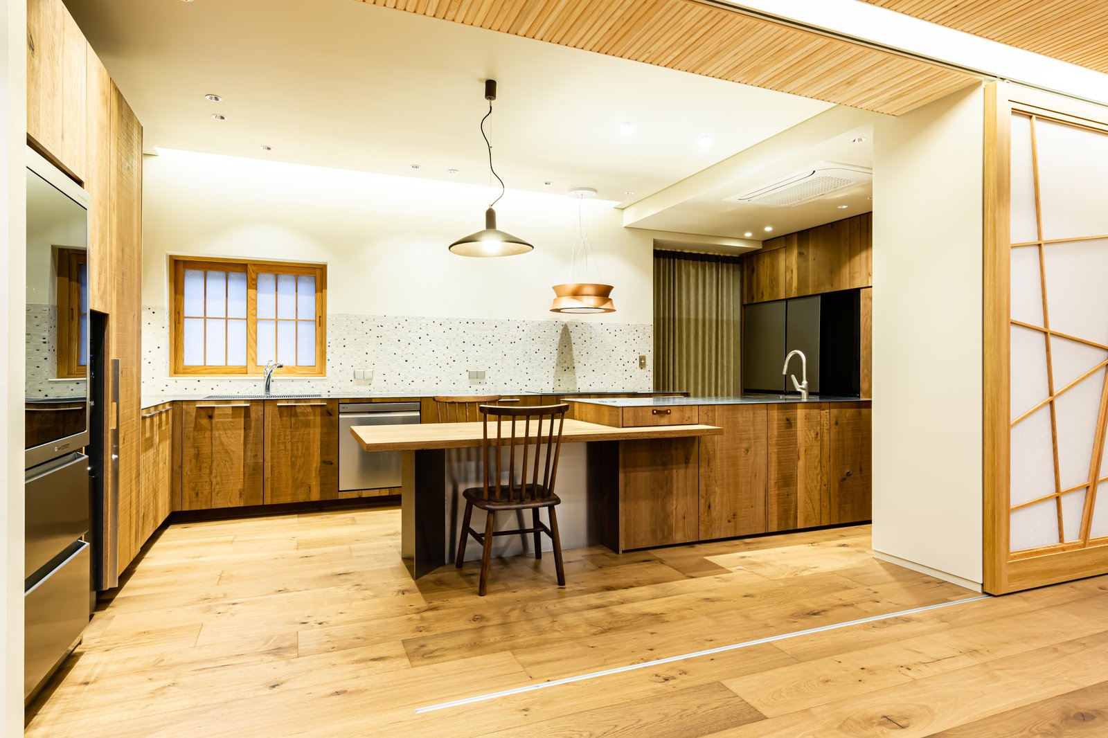 Open kitchen with wood cabinetry, terrazzo backsplash, and a central island beside a shoji sliding door
