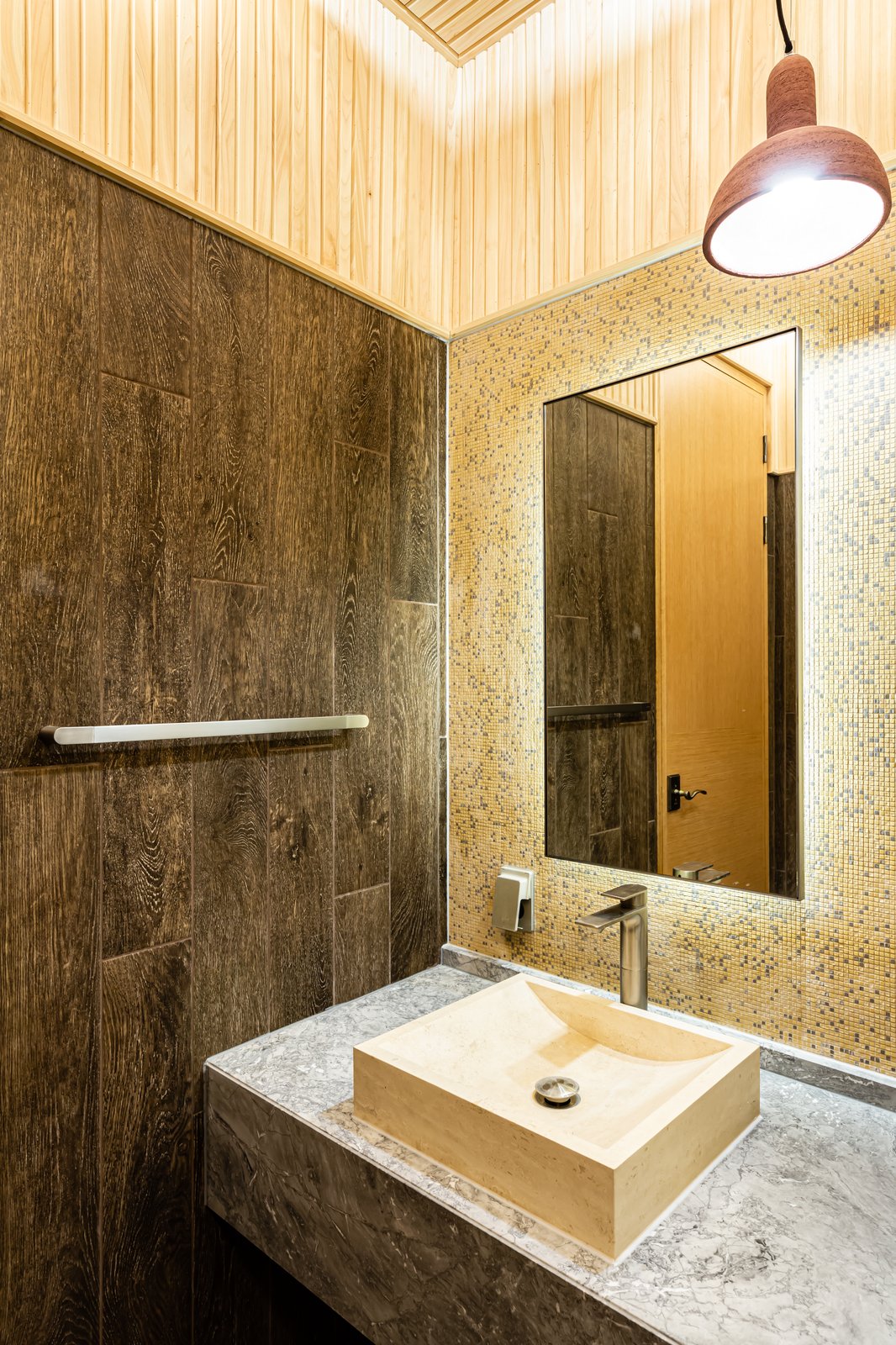 Powder room with a wood-tile accent wall, gold mosaic tile, and a stone vessel sink under a pendant light
