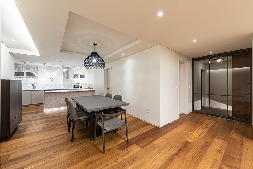 Open-plan dining and kitchen area with wood flooring, a woven pendant light, and dark wood cabinet