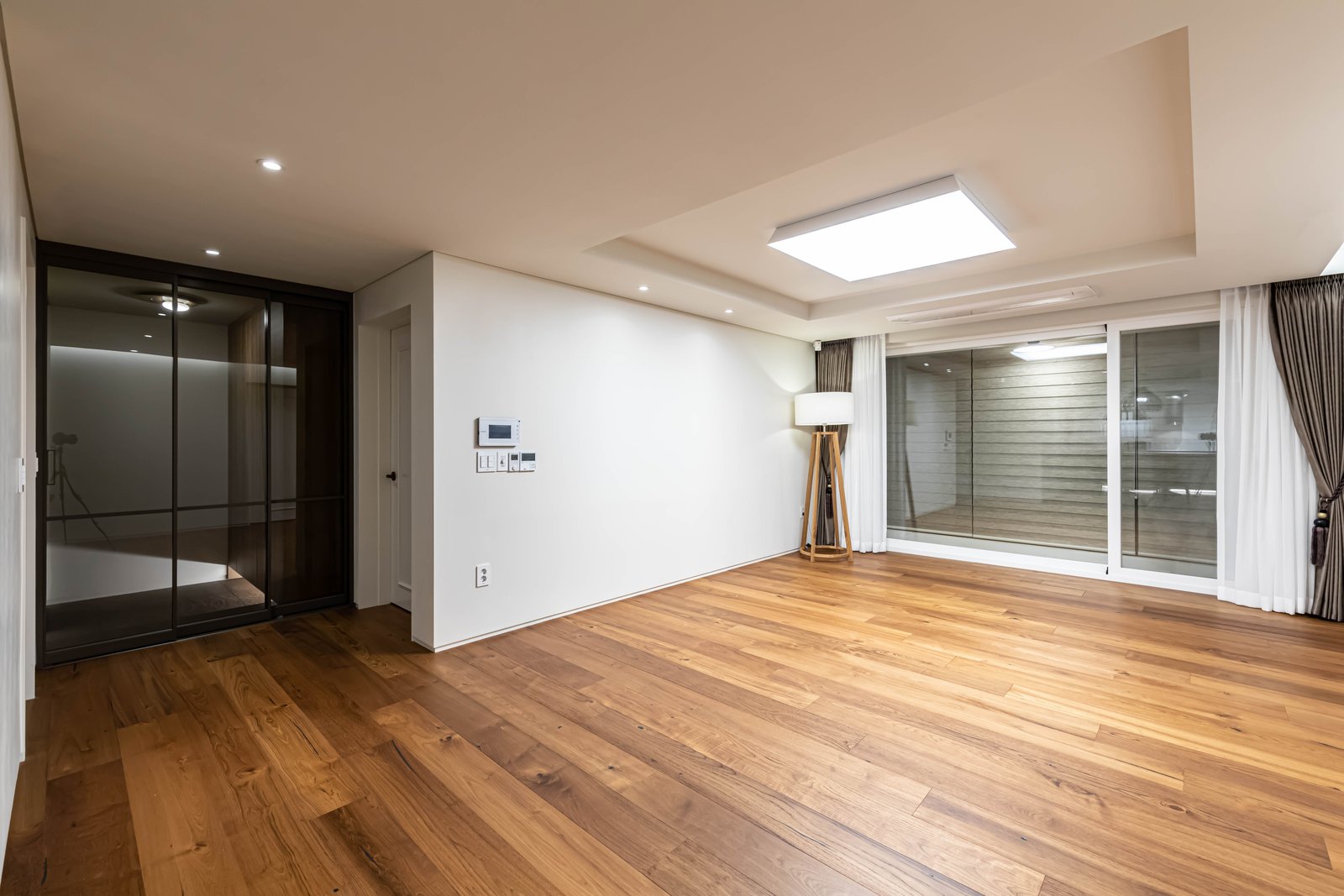 Empty living room with wood flooring, a floor lamp, and glass sliding doors to the balcony