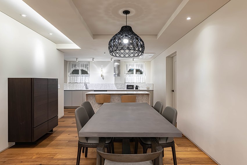 Dining table with woven pendant light and kitchen island beyond