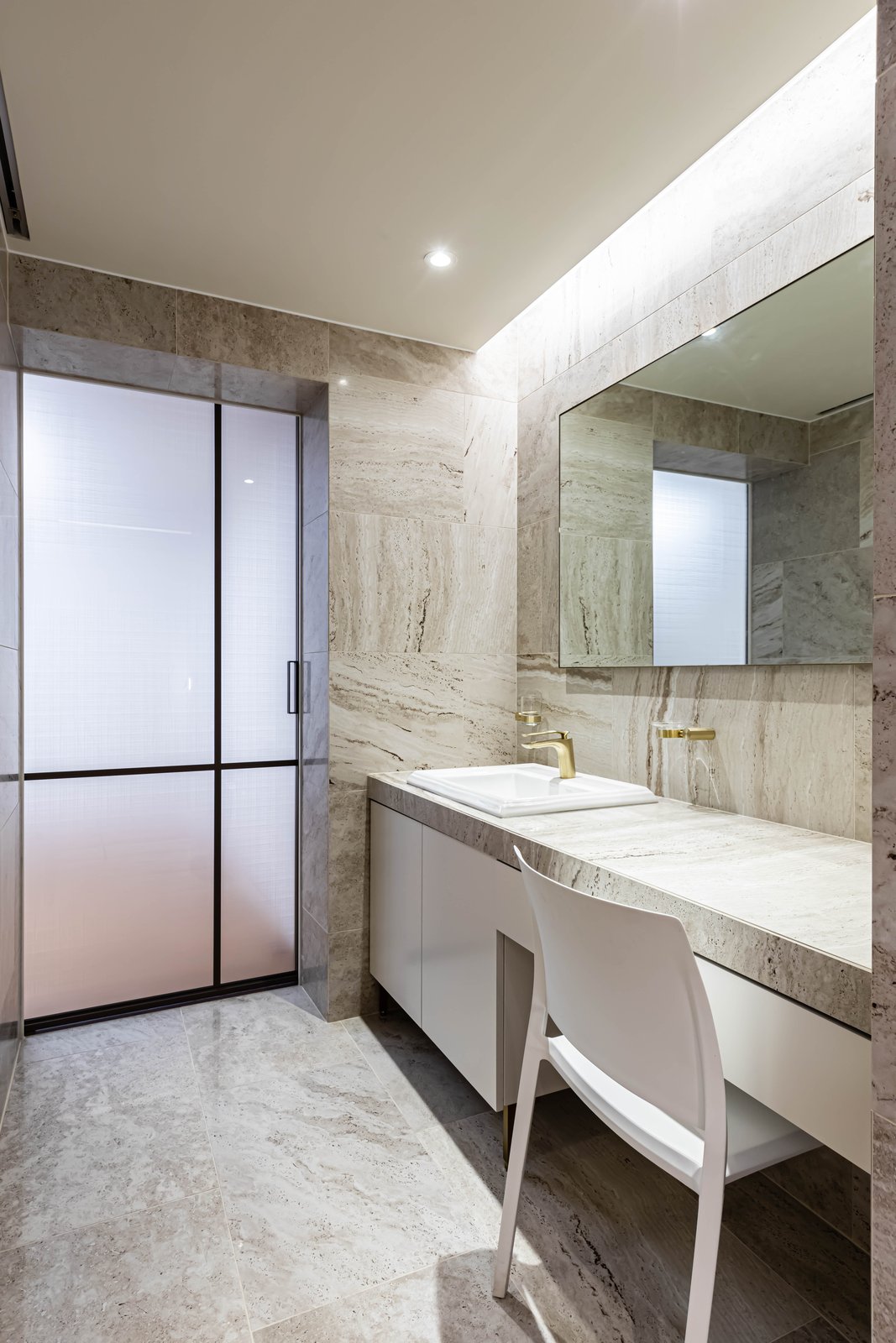 Bathroom vanity with stone countertop, backlit mirror, and white chair