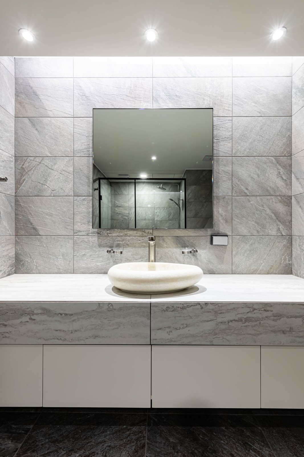 Bathroom vanity with round stone vessel sink and mirror reflecting the glass shower