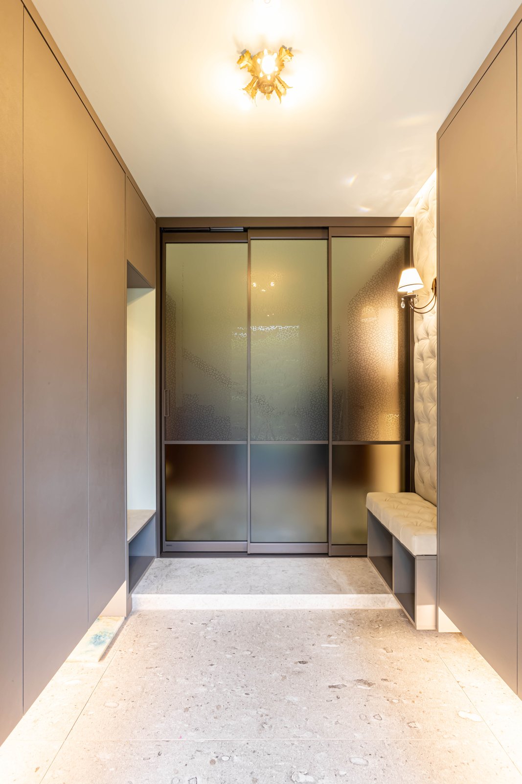 Mudroom with frosted glass sliding doors and a tufted bench beneath a wall sconce