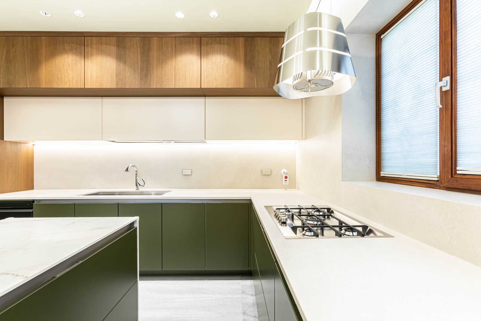 Kitchen with wood cabinetry, stainless steel range hood, and gas cooktop beneath a window