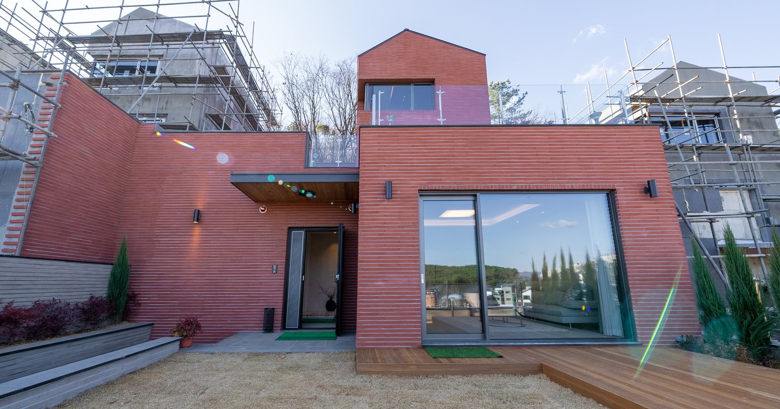 Red brick townhouse exterior with construction scaffolding on either side and an open glass sliding door to a wood deck