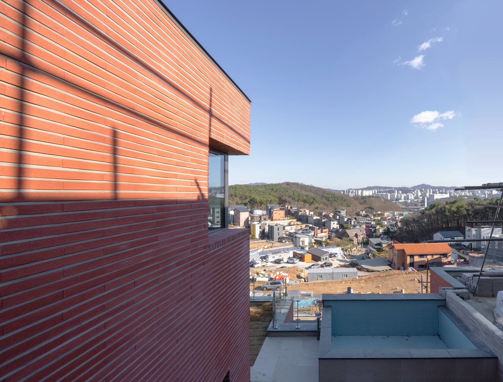 Corner brick facade detail with rooftop terrace and hillside view under blue sky