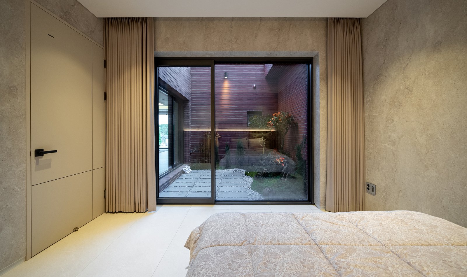 Bedroom with a glass sliding door opening to a small brick-walled courtyard garden