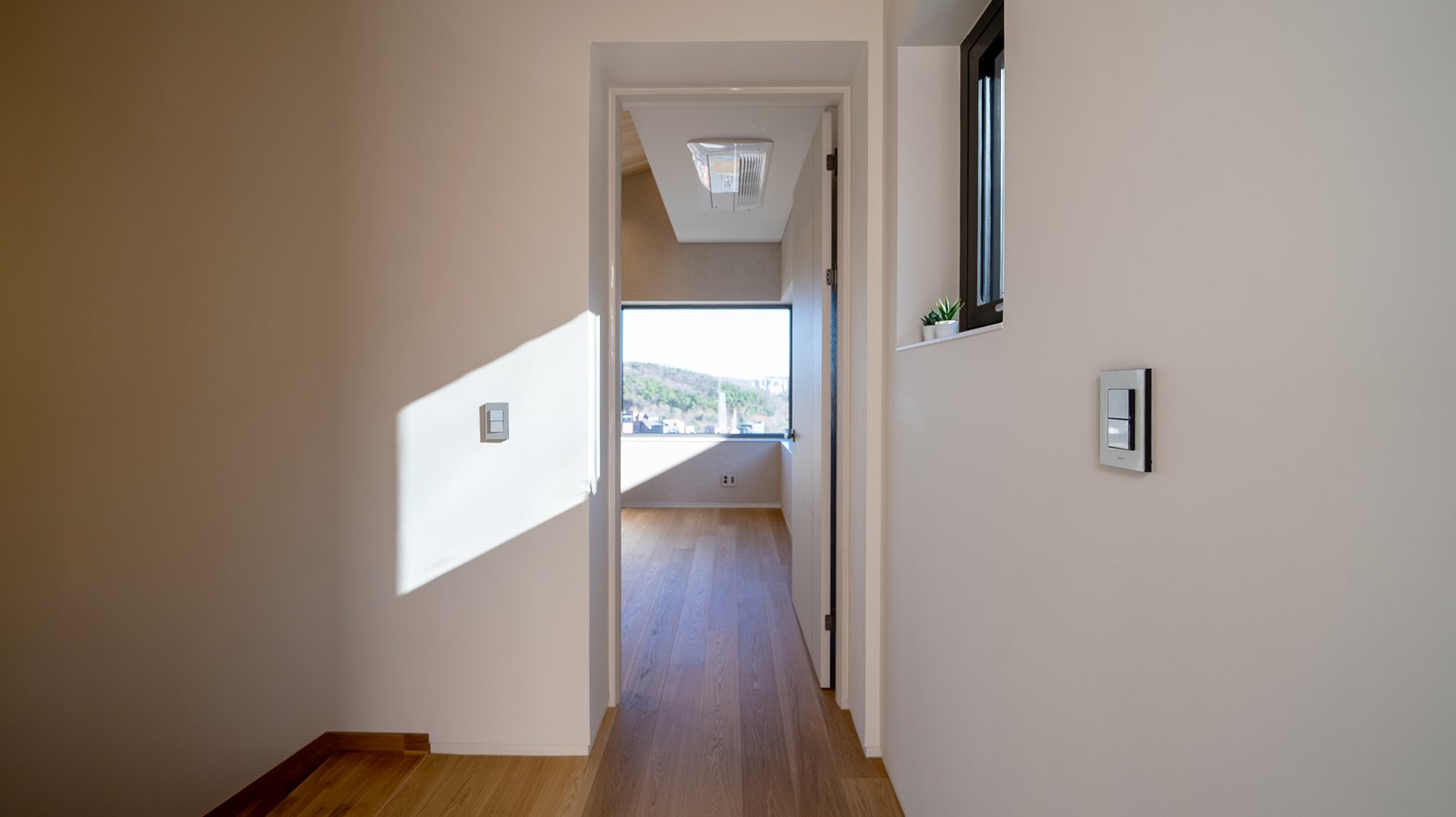 Wood-floored hallway leading to a small room with a wall-mounted light switch panel