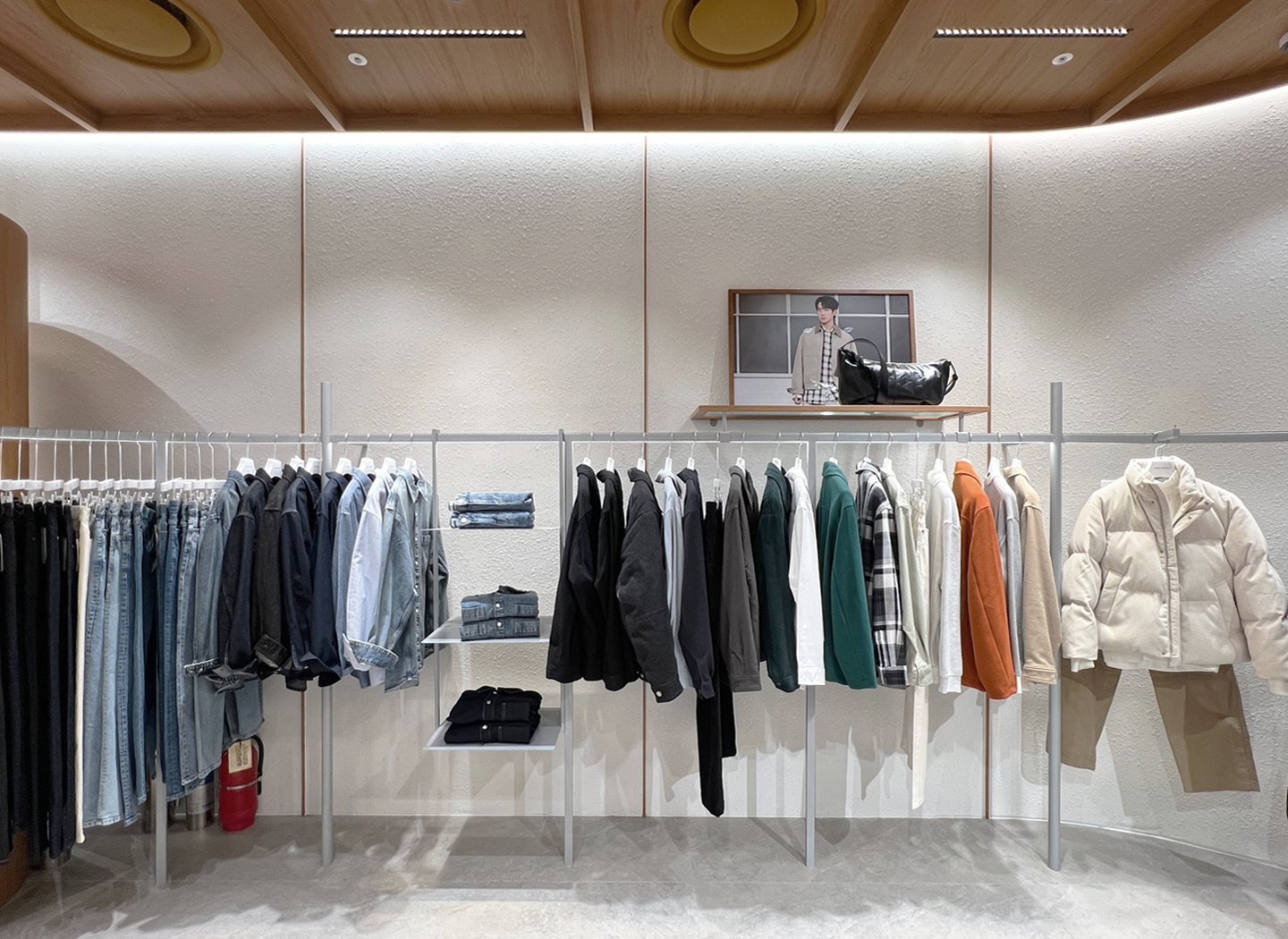 Rear wall clothing rails with denim, knitwear, and outerwear beneath an accessory shelf