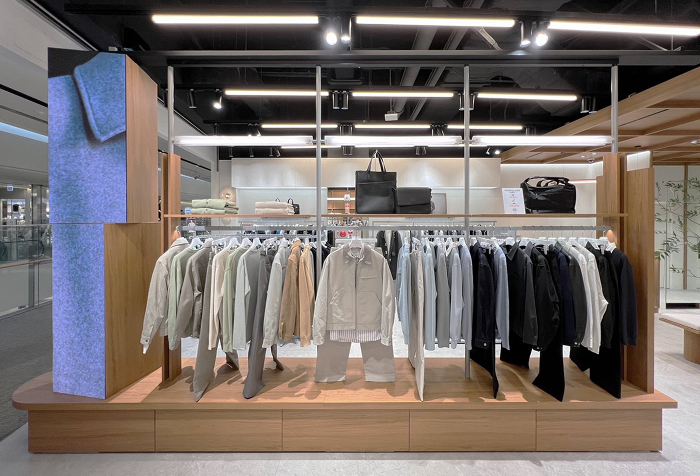 Center island display with jackets, trousers, and a portrait media column
