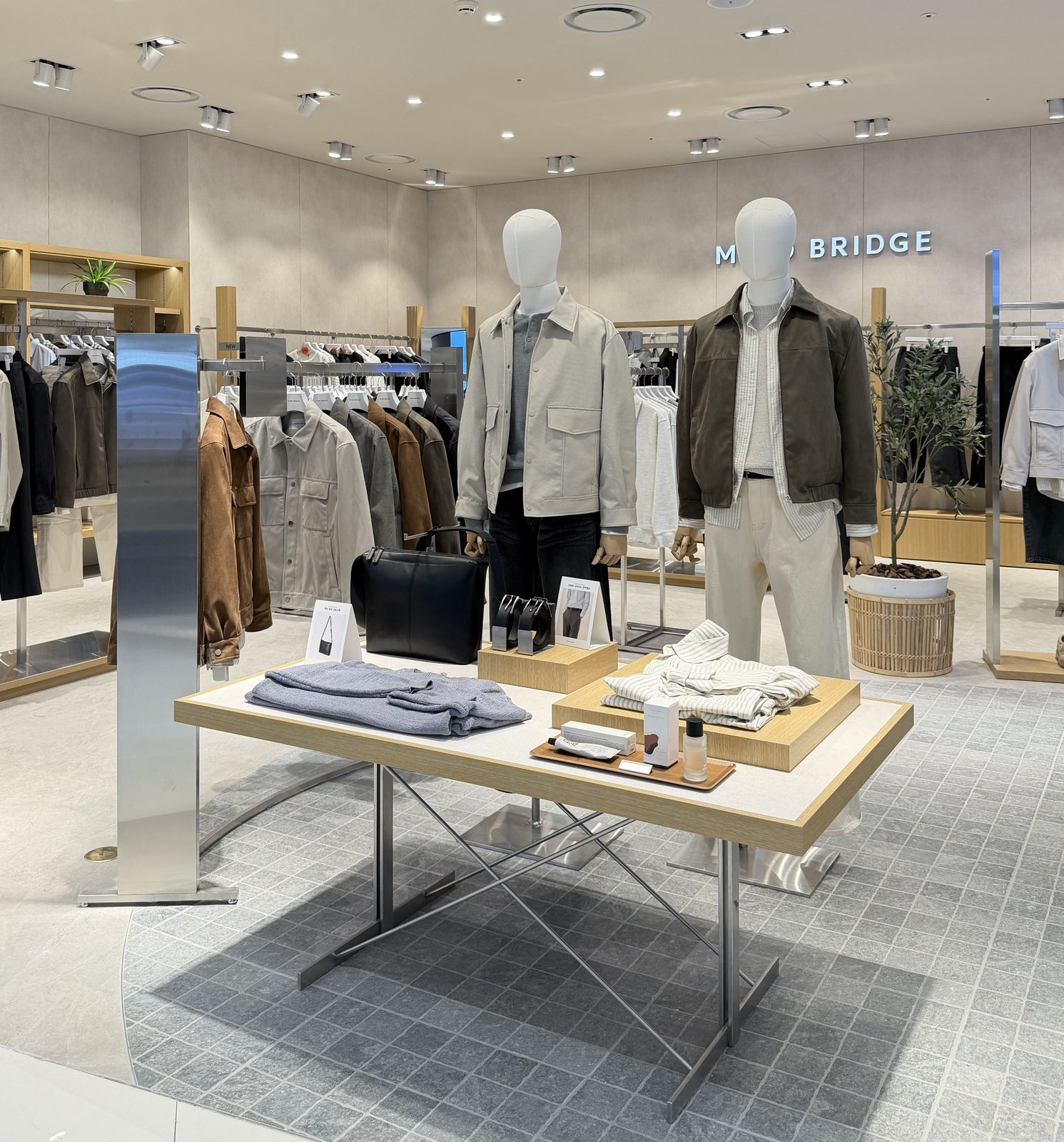 Menswear display table with jackets, bags, and accessories near mannequins